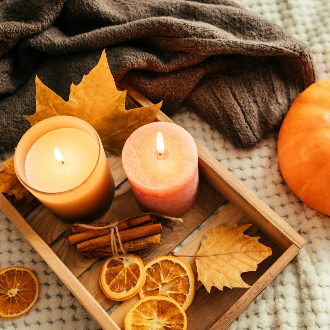 composition of a knitted sweater and autumn home decor. Candles, fallen leaves, pumpkin and cinnamon