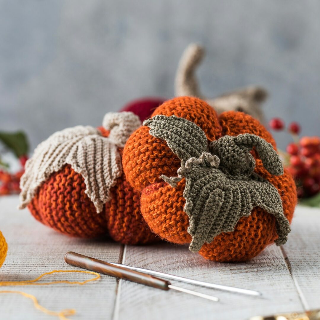 Handmade knitted pumpkins with leaves on white table